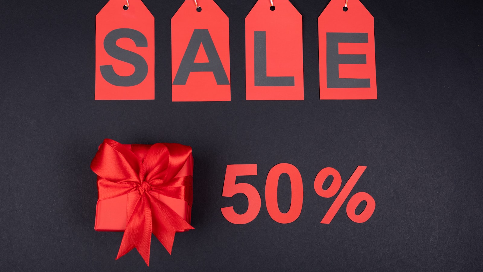 Red SALE tags spelling SALE, a wrapped gift, and a 50 percent mark — merchandising a merchant still has to operate after the click
