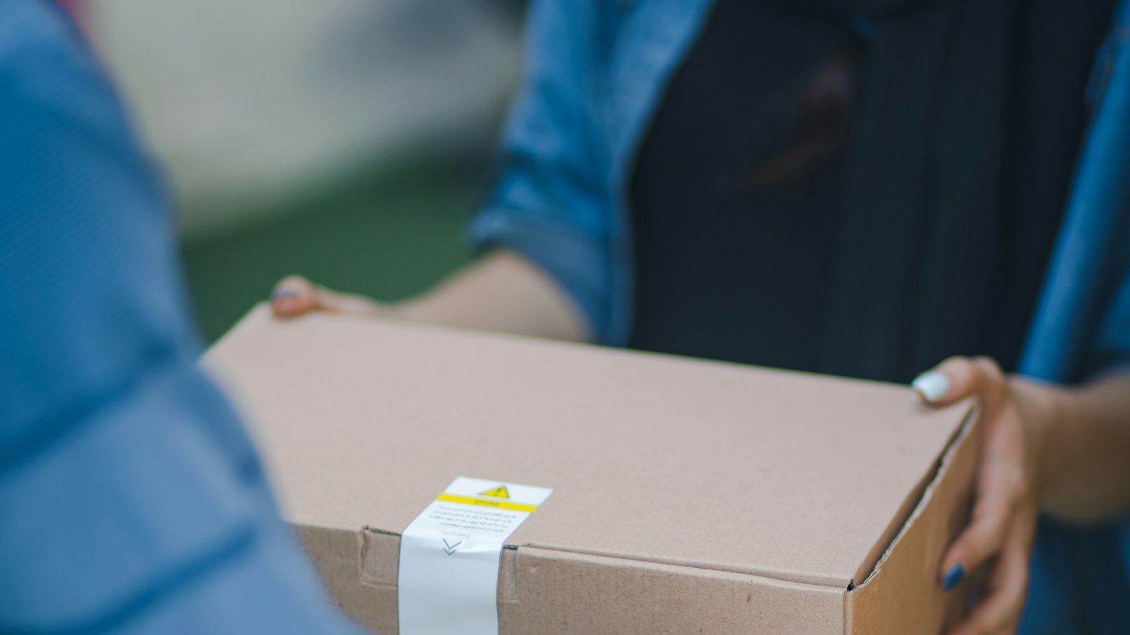 A person handing a sealed cardboard parcel to a customer — what a new Shopify store should install first