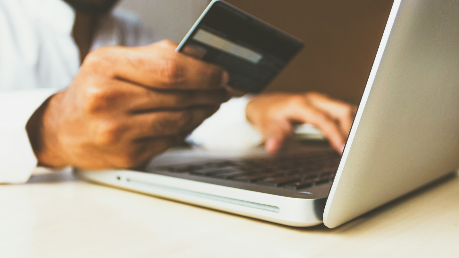 Hands typing on a laptop while holding a payment card — read Shopify app permissions before you grant customer data