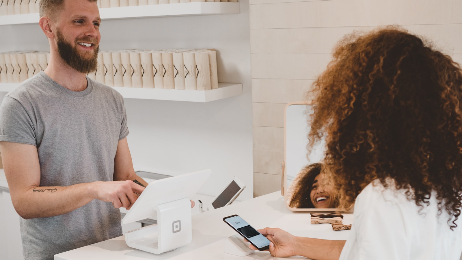 Retail associate at a tablet checkout with a customer paying by phone — pick one Shopify upsell surface